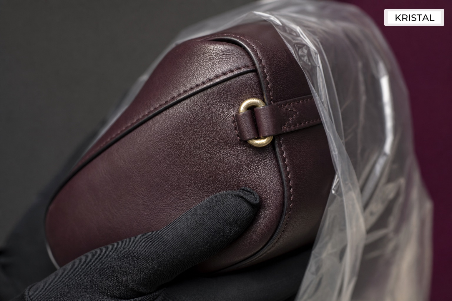 Gloved hand checking the corner, seam and strap attachment of a shoulder bag in a protective sleeve
