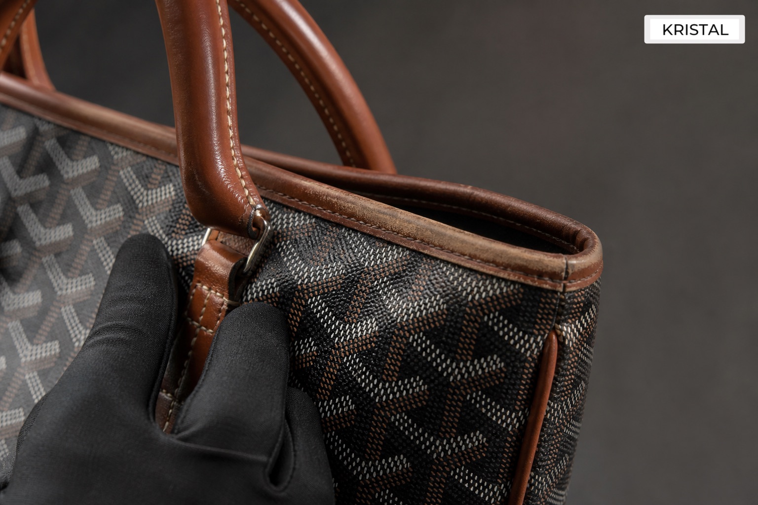 Editorial inline image showing close inspection of a Goyard-style tote handle, top edge, and coated canvas during valuation review in Malaysia