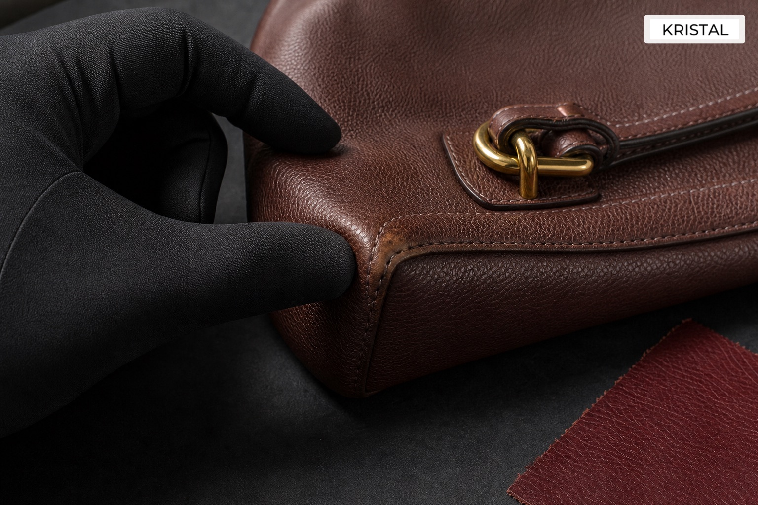 Gloved hand checking a handbag corner and handle base against a charcoal surface