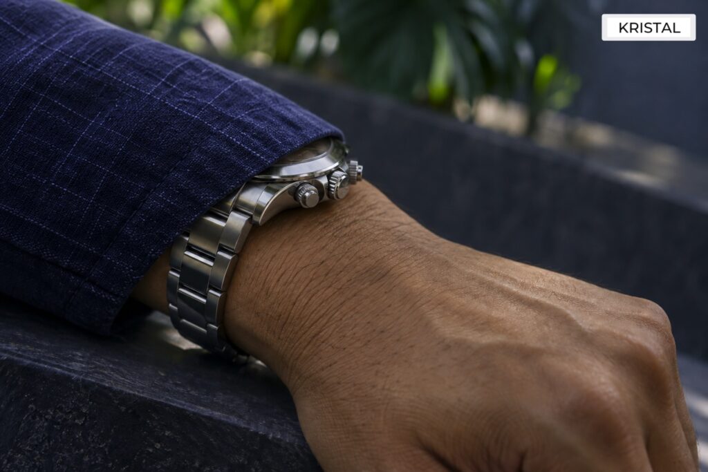 Illustrative steel chronograph worn partly beneath a blue cuff