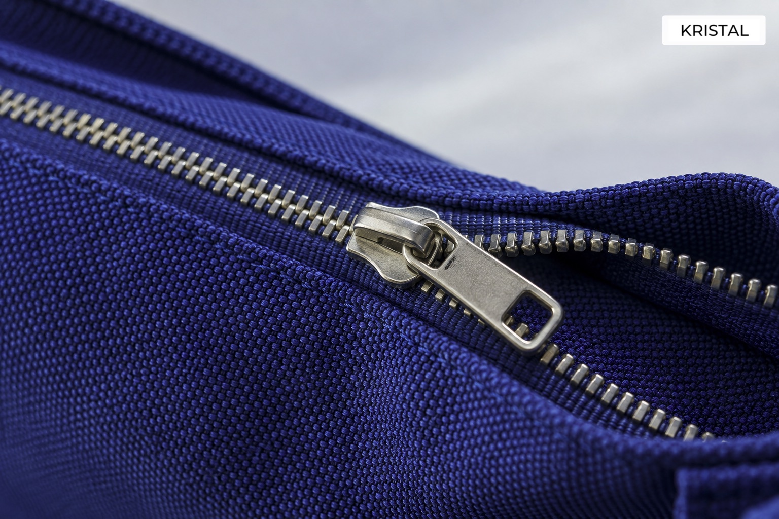 Conceptual close-up of a zipper slider and interlocking teeth on blue fabric